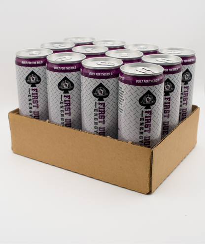 A cardboard tray holding 12 aluminum cans of First Due Energy with purple and silver diamond plate texture labels, photographed on a white studio background.